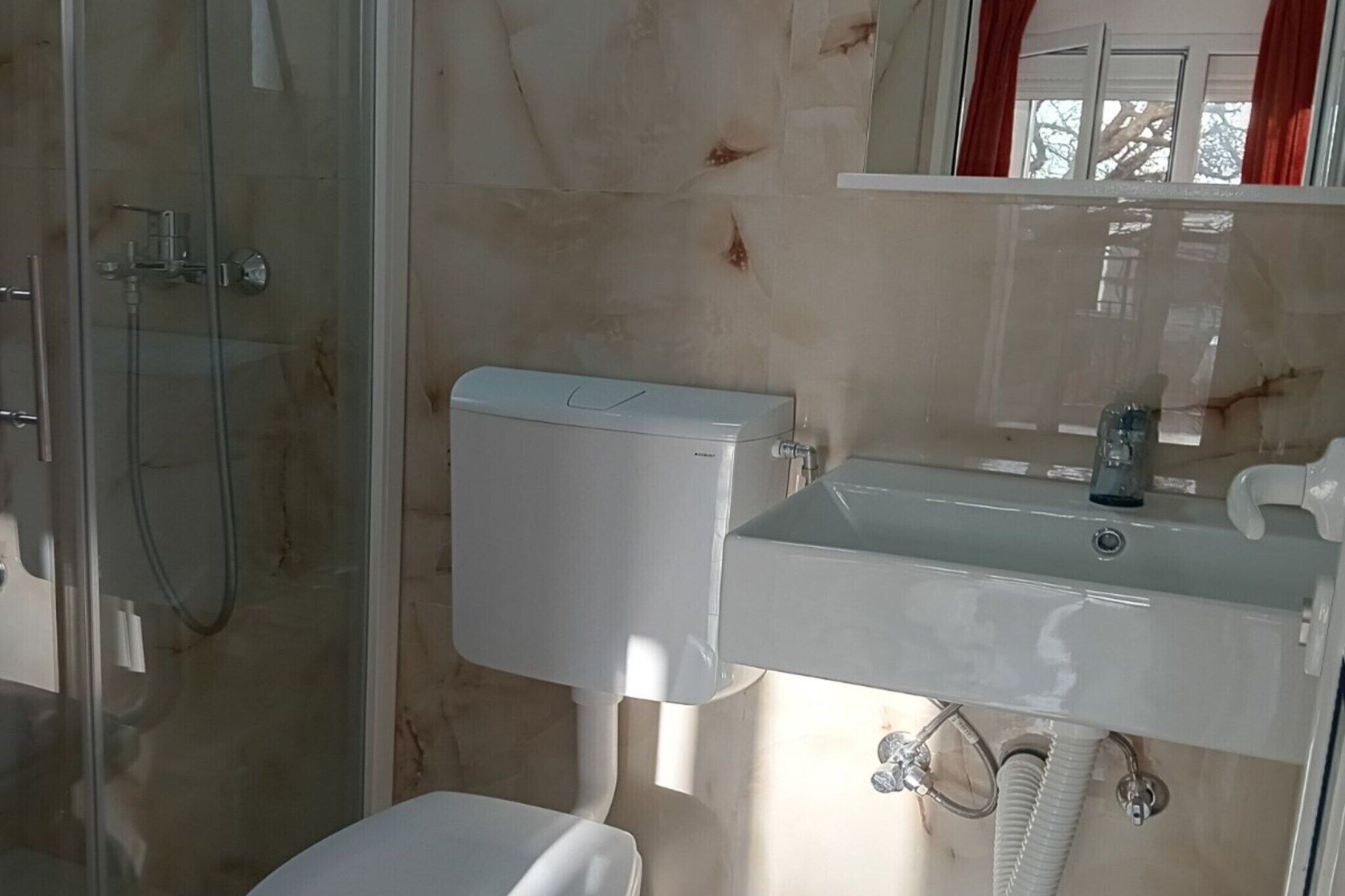 A bathroom with a glass-enclosed shower, a white toilet, and a sink with a mirror above it.