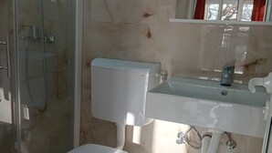 Un baño con ducha de mampara de vidrio, inodoro blanco y lavamanos con espejo arriba.