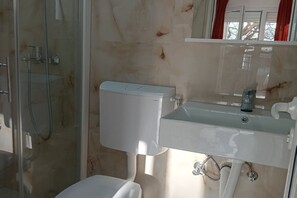 Ein Badezimmer mit Duschkabine, Toilette in Weiß und Waschbecken mit Spiegel darüber.