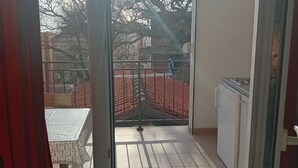 Un balcón con una mesa, sillas, una reja metálica y un refrigerador.