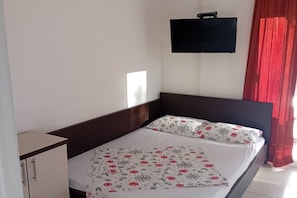 A single bed with a patterned bedspread, a bedside table, a flat-screen TV mounted on the wall, and a red curtain. - Superior Studio Apartment with Sea View and Terrace (Sutomore)