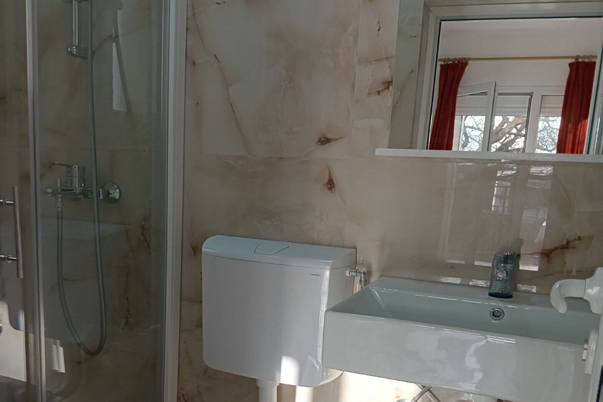 Une salle de bain avec une douche à parois de verre, des toilettes blanches et un lavabo avec un miroir au-dessus.