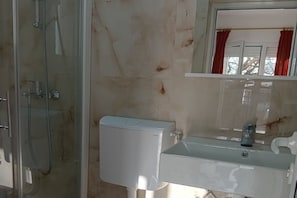 Une salle de bain avec une douche à parois de verre, des toilettes blanches et un lavabo avec un miroir au-dessus.