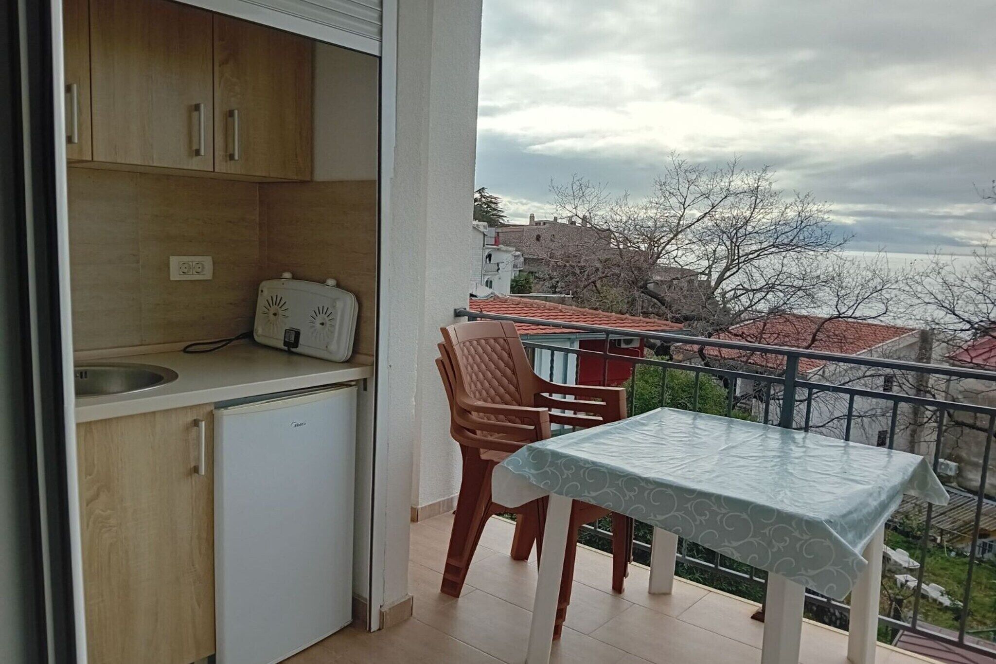 Un balcó amb taula i caires, una petita cuina amb nevera i vista a la ciutat.