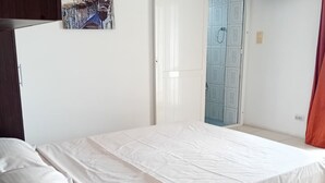 Een slaapkamer met een bed, een houten nachtkastje, een witte muur en een deur naar een badkamer.