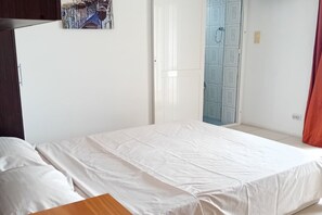 Ein Schlafzimmer mit einem Bett, einem Nachttisch aus Holz, einer weißen Wand und einer Tür zu einem Badezimmer.