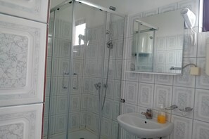 Ein Badezimmer mit Duschkabine aus Glas, Waschbecken mit Spiegel und Wandhaartrockner.