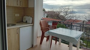 Een balkon met een tafel en stoelen, een kleine kitchenette en uitzicht op gebouwen en bomen.