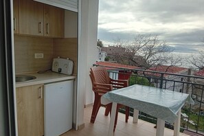 Ein Balkon mit Tisch und Stühlen, eine kleine Küchenzeile und Blick auf Gebäude und Bäume.