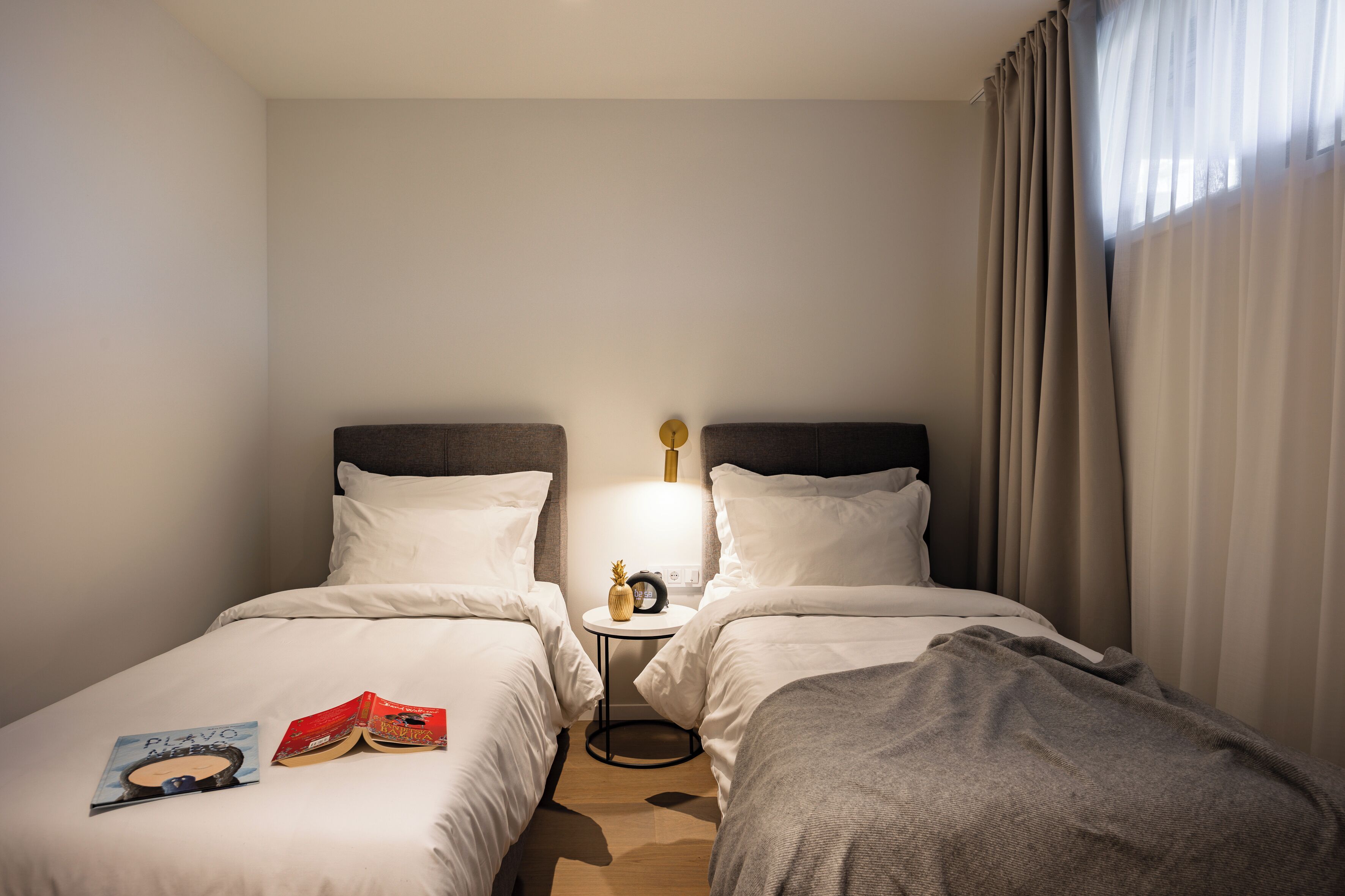 A hotel room with two single beds, a bedside table with a lamp, and a window with curtains.