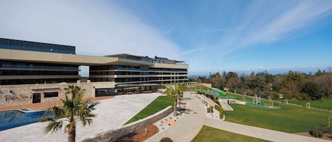 A hotel with a swimming pool, outdoor seating, and a view of the mountains.