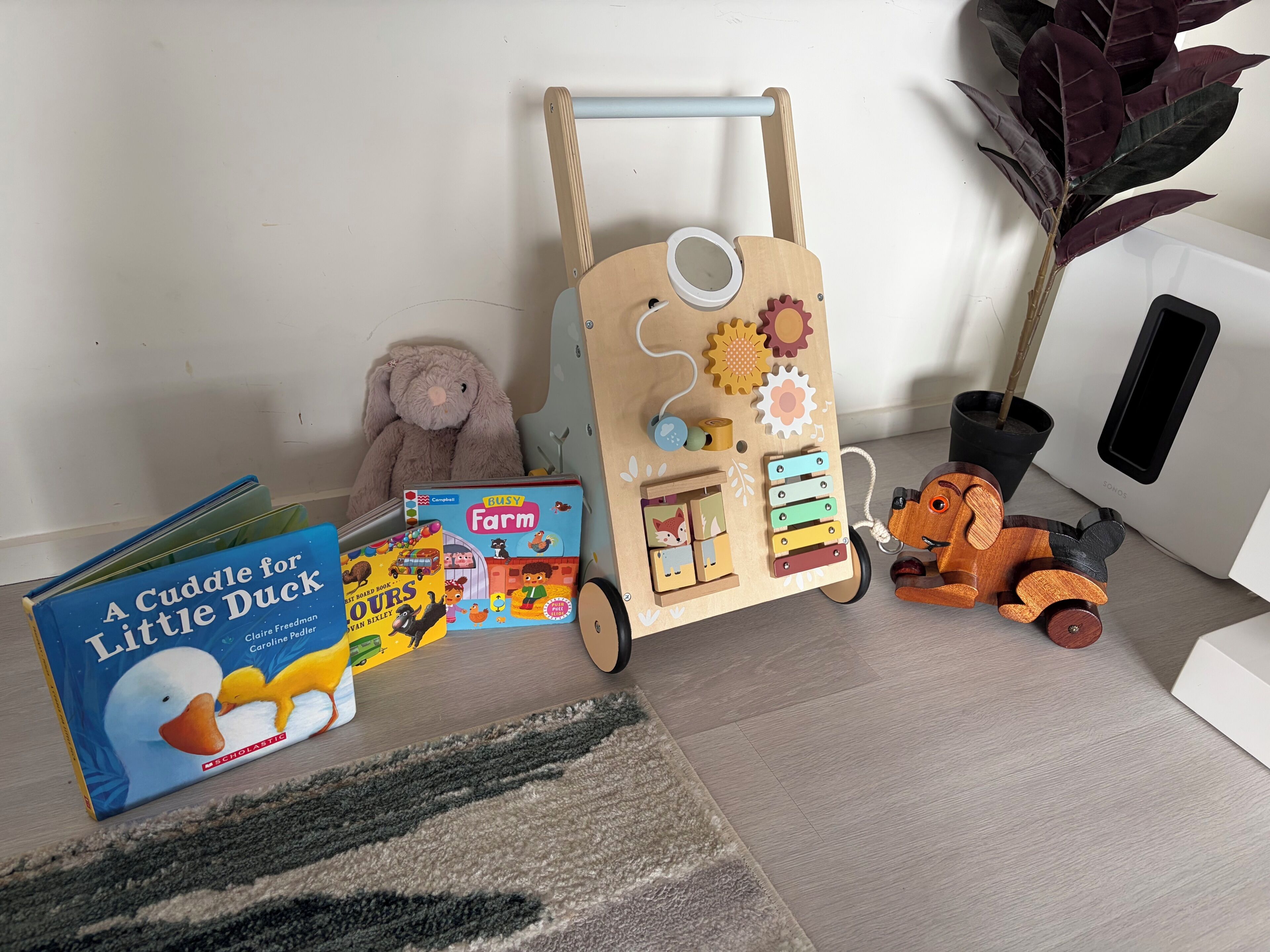 A room with a wooden play area, a plush toy, a book, and a plant.