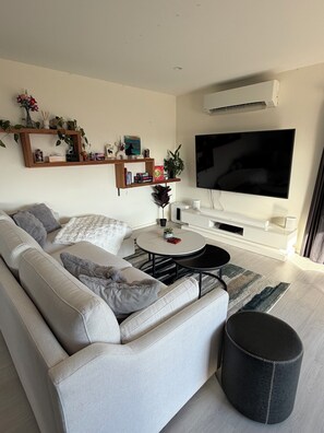 Ein modernes Wohnzimmer mit Sofa, Couchtisch, Hocker und einem Flachbildfernseher.