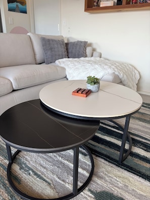 Ein Wohnzimmer mit einer Couch, einem runden Couchtisch und einer kleinen Topfpflanze.