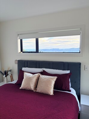A bed with a dark headboard, two pillows, and a red bedspread.