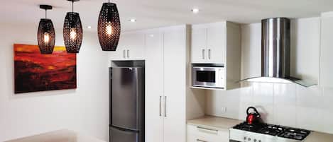 Eine moderne Küche mit Edelstahl-Kühlschrank, Mikrowelle und Gasherd. Über der Arbeitsplatte hängen Pendelleuchten.