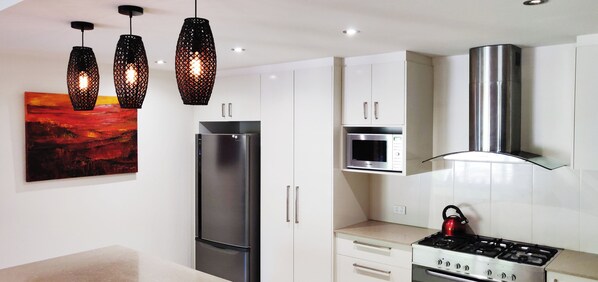 A modern kitchen with a stainless steel refrigerator, microwave, and gas stove. There are pendant lights above the counter.