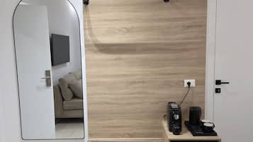 Un dormitorio moderno con un panel de madera en la pared, una mesita de noche con cafetera, un espejo y una cama con toalla blanca.