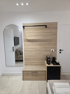 A modern bedroom with a wooden panel wall, a bedside table with a coffee maker, a mirror, and a bed with a white towel. - The Story Hotel (Tirana)