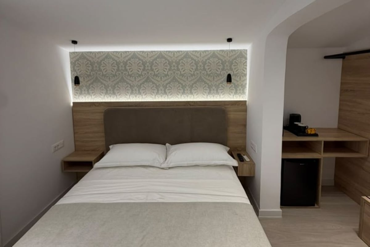 Una habitación de hotel moderna con una cama grande, un cabecero de madera, una mesita de noche y un estante empotrado.