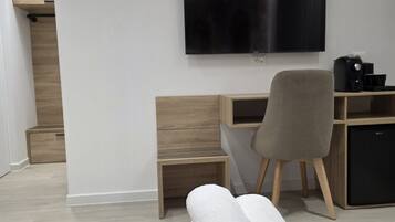 Una habitación de hotel moderna con una televisión de pantalla plana montada en la pared, un escritorio de madera, una silla y una toalla enrollada en el suelo.