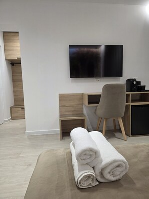 Una habitación de hotel moderna con una televisión de pantalla plana montada en la pared, un escritorio de madera, una silla y una toalla enrollada en el suelo.
