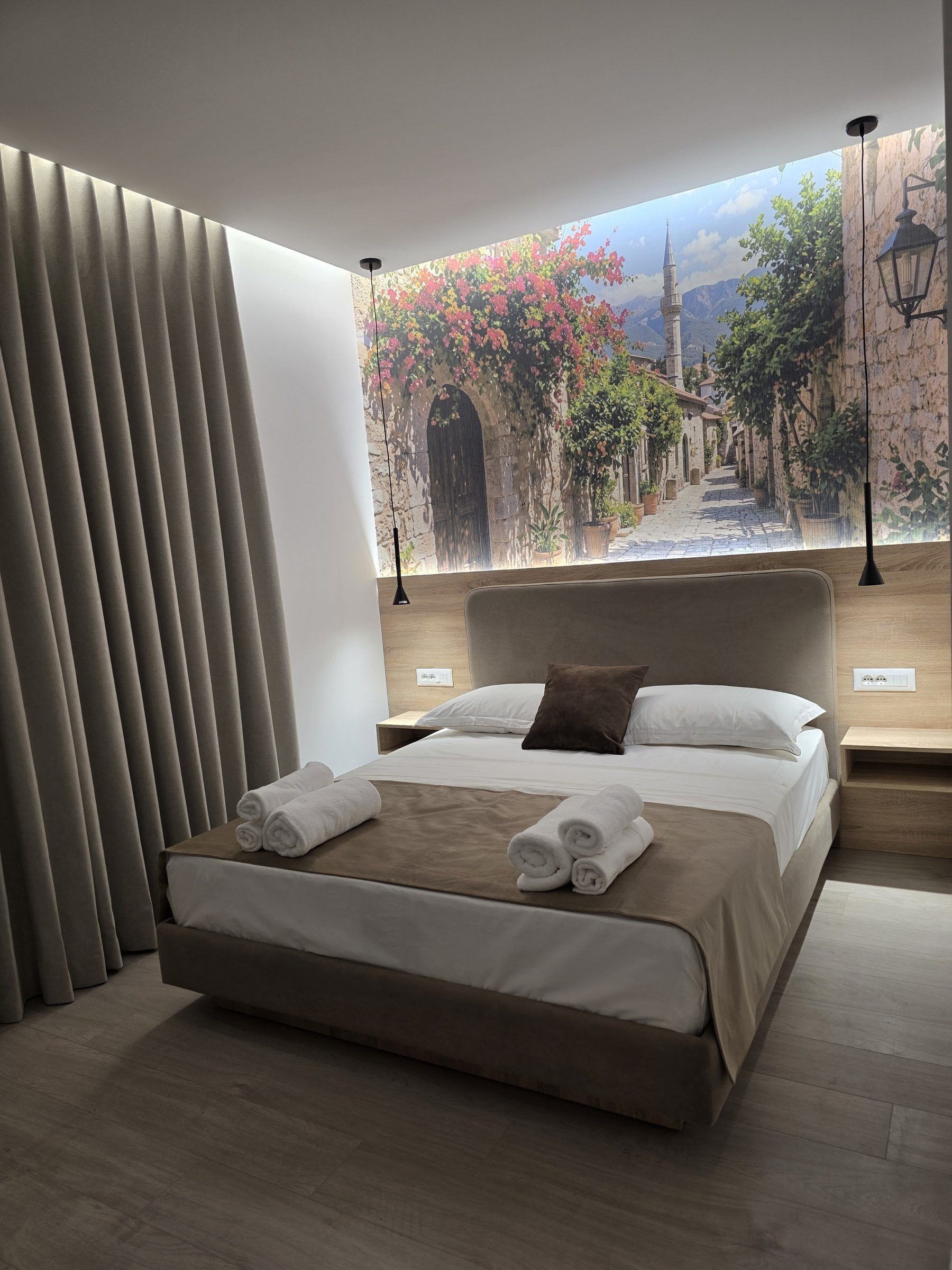 A modern bedroom with a large bed, a view of a street scene through a window, and a wall-mounted lamp.