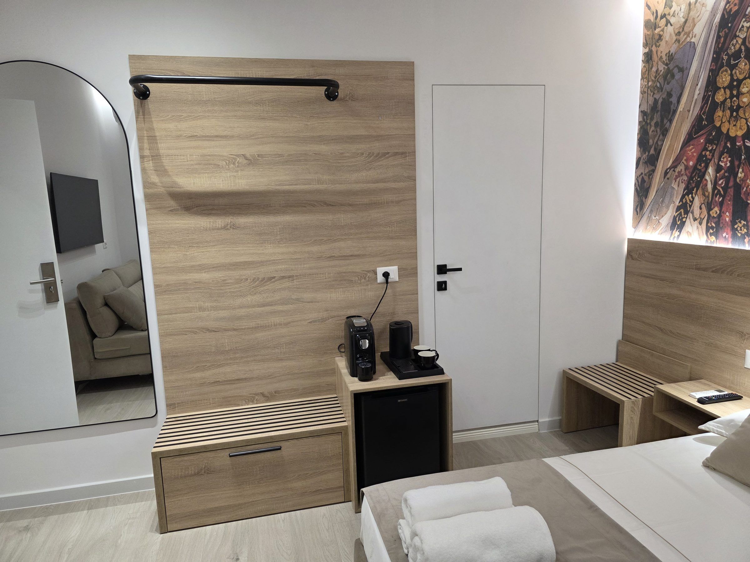 Un dormitorio moderno con cabecera de madera, una mesita de noche con cafetera, un mueble pequeño y una cama con ropa blanca.