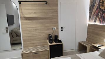 Un dormitorio moderno con cabecera de madera, una mesita de noche con cafetera, un mueble pequeño y una cama con ropa blanca.
