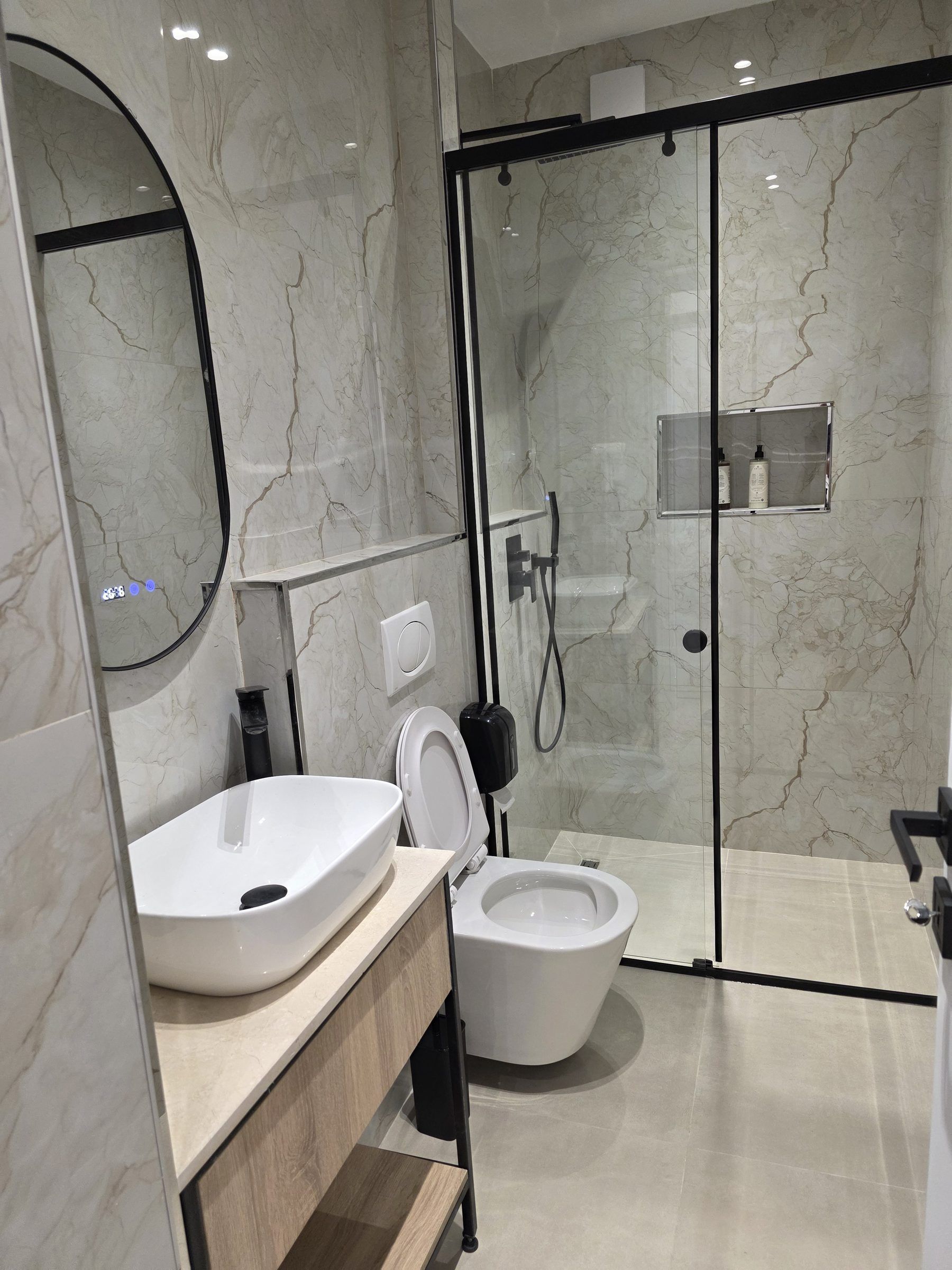 A modern bathroom with a marble vanity, a toilet, and a glass-enclosed shower area.