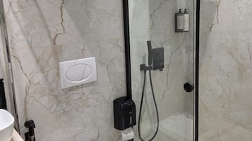 Un baño moderno con ducha envuelta en vidrio, inodoro y pared de mármol.