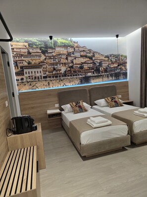 A hotel room with two beds, a wooden bench, a view of a coastal town, and a modern lamp. - The Story Hotel (Tirana)