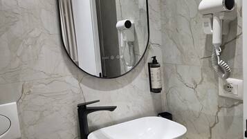 Un baño con pared de mármol, un lavamanos blanco, un grifo negro, un espejo redondo y un secador de pelo montado en la pared.