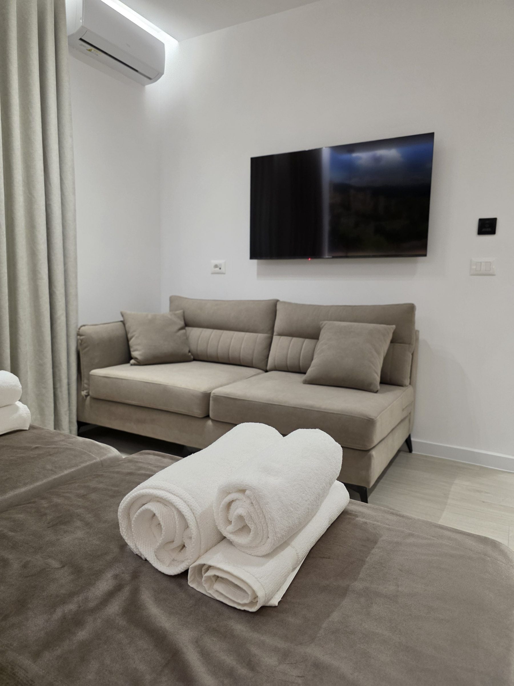 Una habitación moderna con sofá, televisor de pantalla plana en la pared y cama con toallas dobladas.