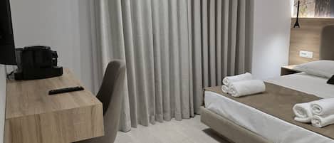 Una habitación de hotel moderna con cama, escritorio, silla, televisión y ventana con cortinas.