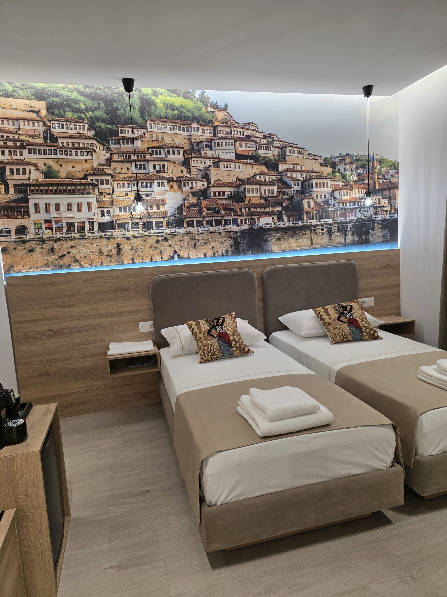 Habitación de hotel con dos camas, piso de madera, vista a un pueblo costero y una cafetera.