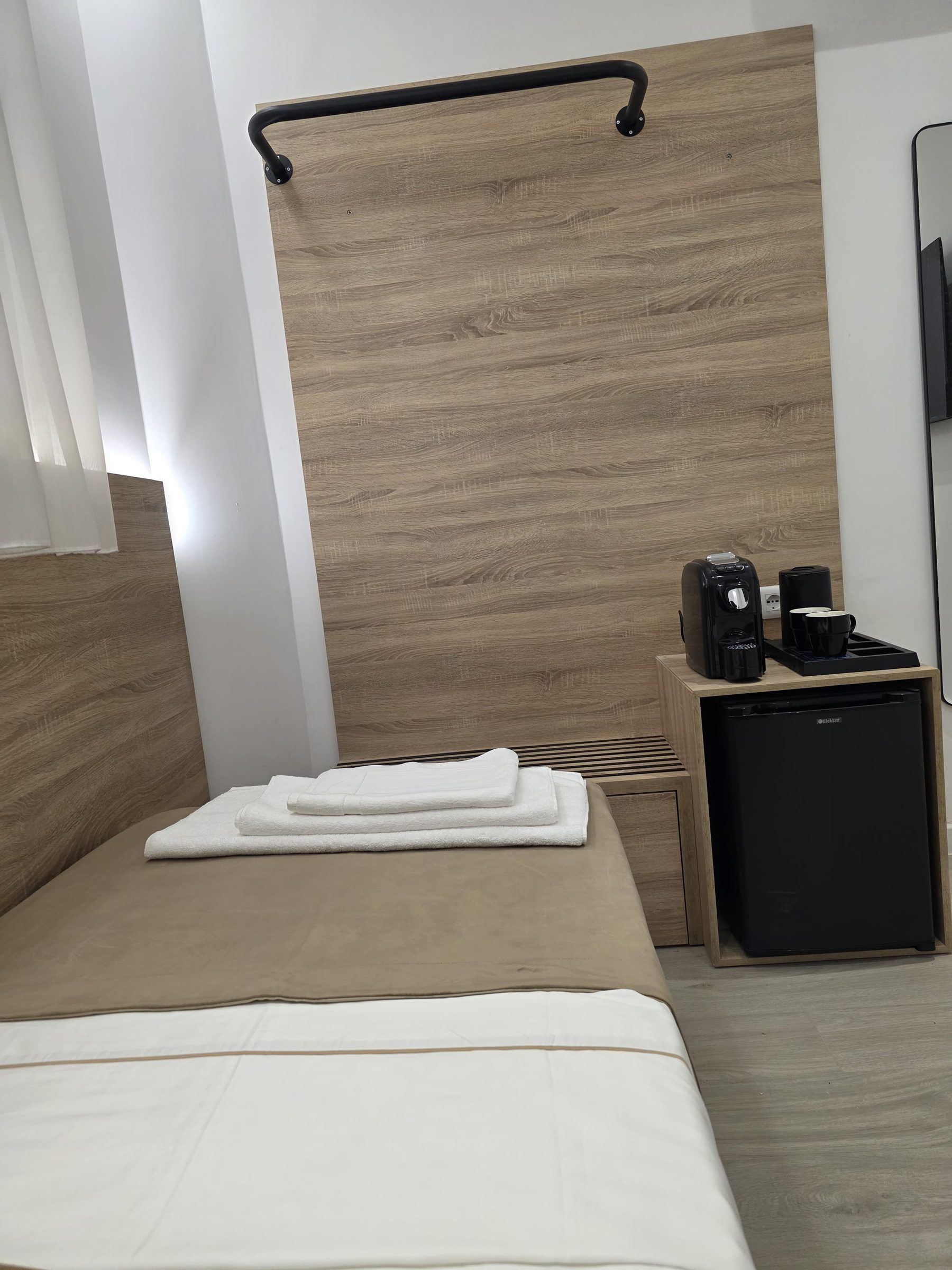 Habitación de hotel con una cama, un refrigerador pequeño, cafetera y pared de paneles de madera.