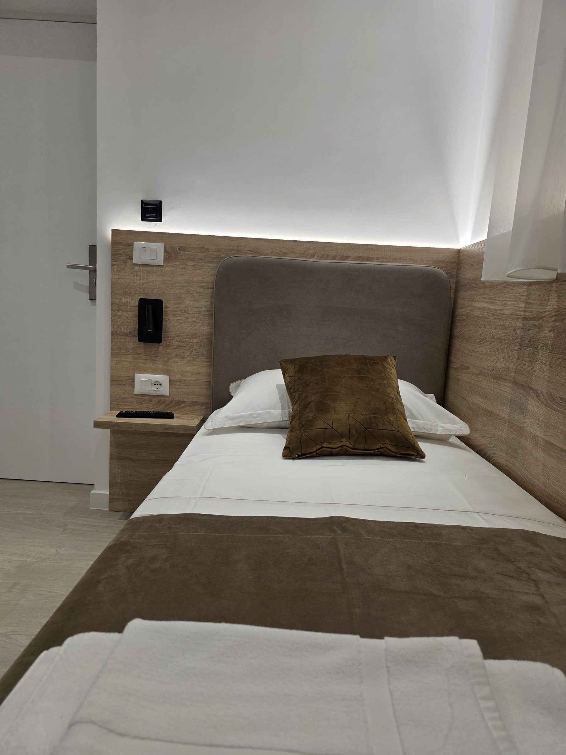 Habitación de hotel moderna con cama, mesita de noche y panel de control en la pared.