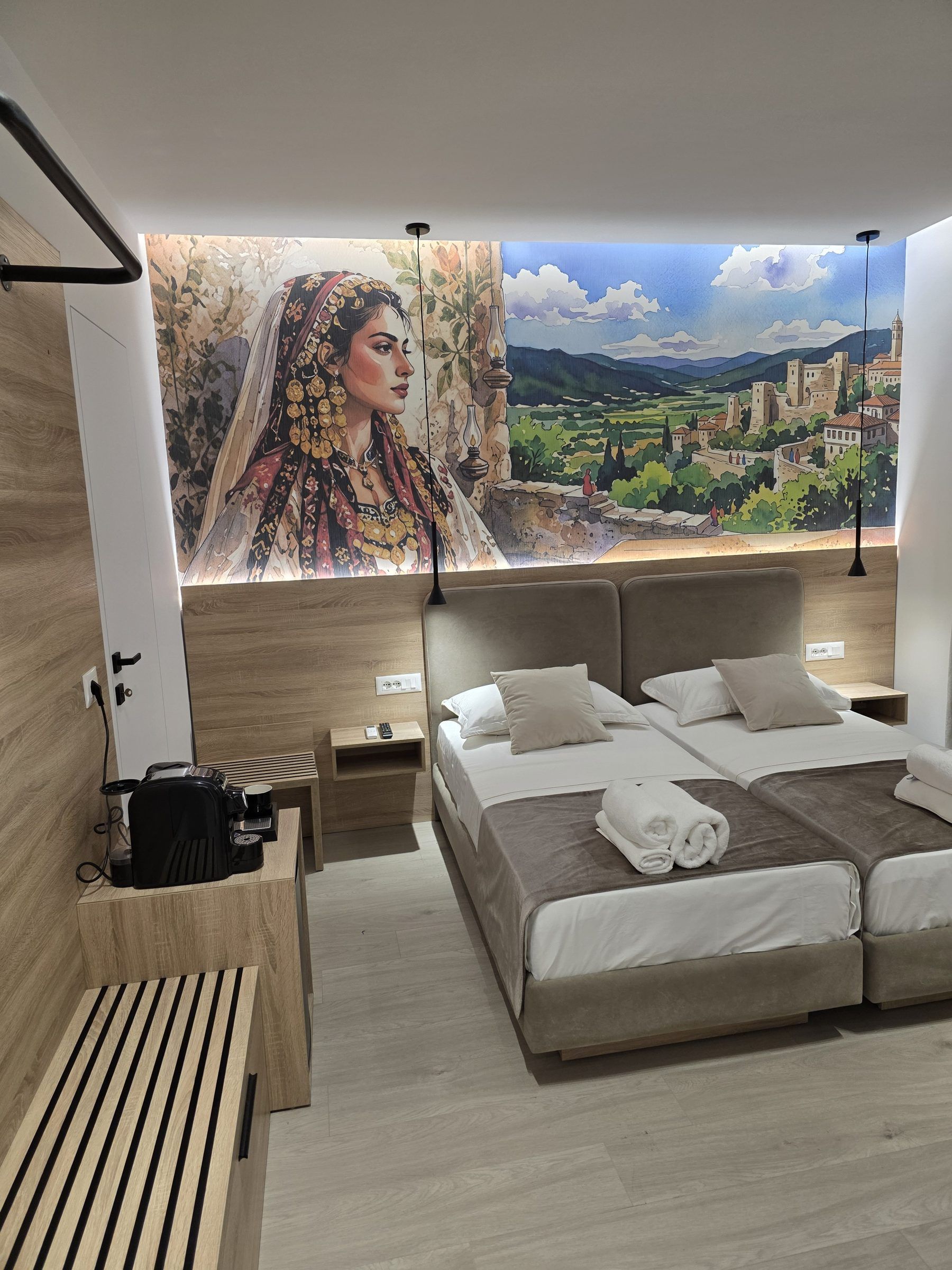 A modern bedroom with a large bed, bedside tables, a bench, and a mural of a landscape and a woman.