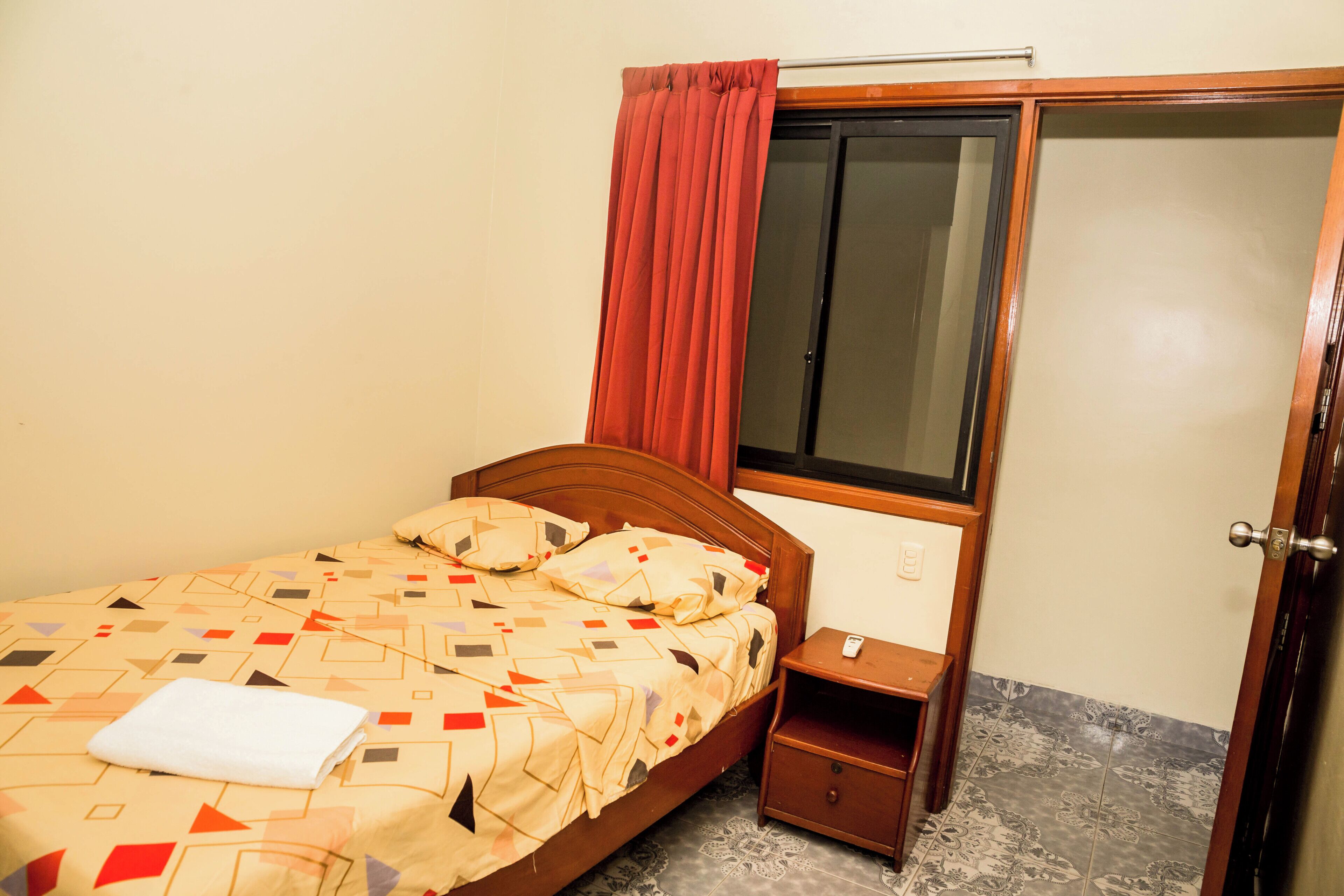 Um quarto com cama, mesa de cabeceira, guarda-roupa e janela com cortinas.