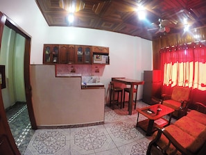 A kitchen with a built-in counter, wooden cabinets, and a tiled floor. There is a dining area with a table and chairs, and a red sofa.