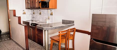 Una cocina compacta con gabinetes de madera, un refrigerador de acero inoxidable, un microondas y un lavabo.
