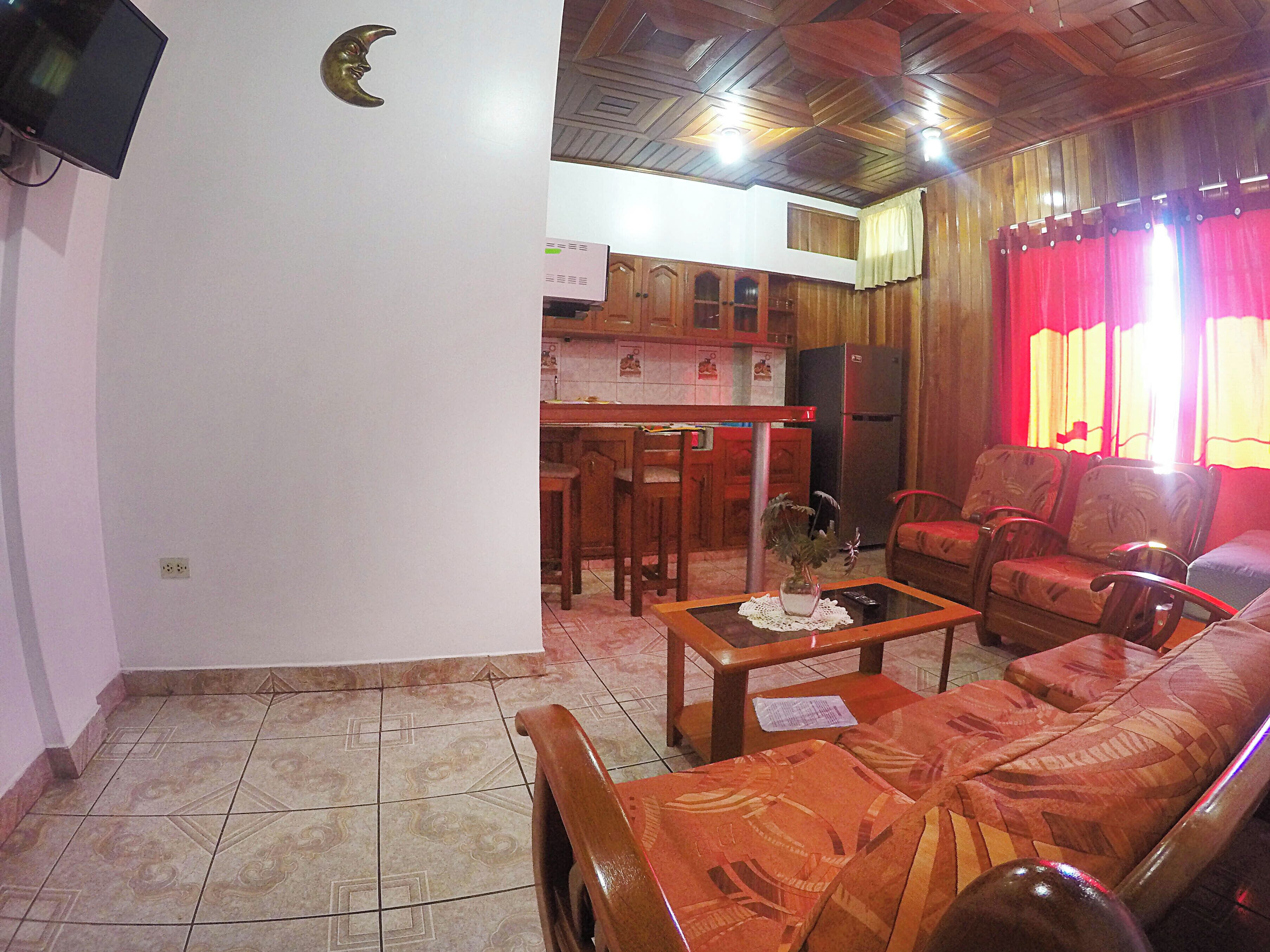 Uma sala de estar com um sofá, uma mesa de centro e uma televisão fixada na parede.