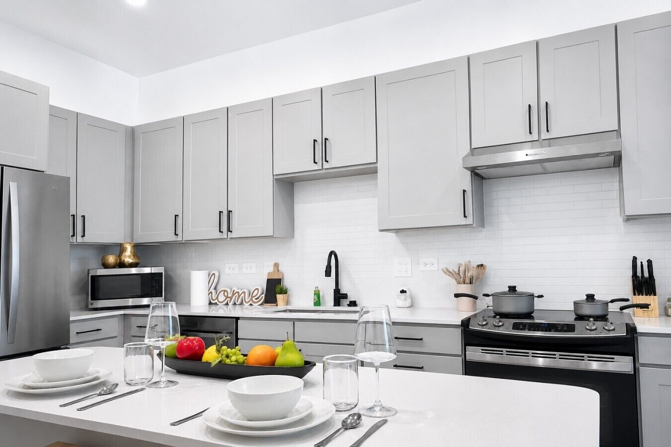 A modern kitchen with grey cabinets, stainless steel appliances, and a central island with dining setup.