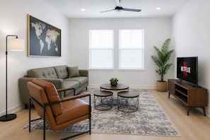 Una sala de estar moderna con sofá, sillón, mesa de centro, televisor y un mapa del mundo en la pared.