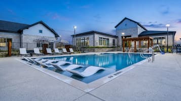 A swimming pool with lounge chairs, a covered seating area, and a building with a stone facade.