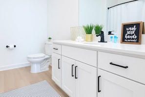 Un baño moderno con inodoro, muebles blancos y encimera con artículos de aseo.