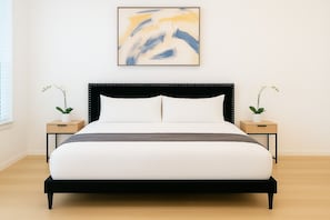 Un dormitorio moderno con un cabecero tapizado en negro, ropa de cama blanca y dos mesitas de noche con orquídeas en macetas.