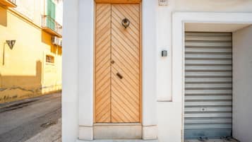 A building entrance with a wooden door featuring a chevron pattern, a metal doorbell, and a metal garage door to the right.