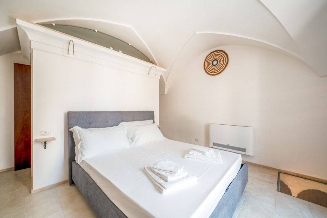 A modern bedroom with a large bed, a bedside table, and a wall-mounted light fixture.